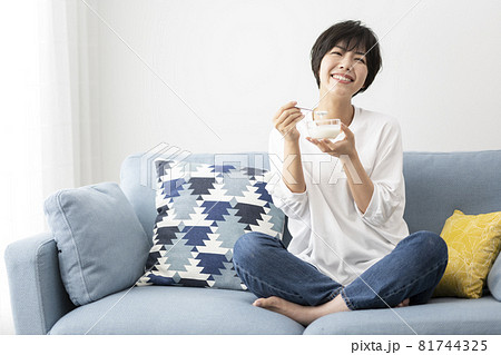 部屋のソファーでヨーグルトを食べる若い女性 81744325
