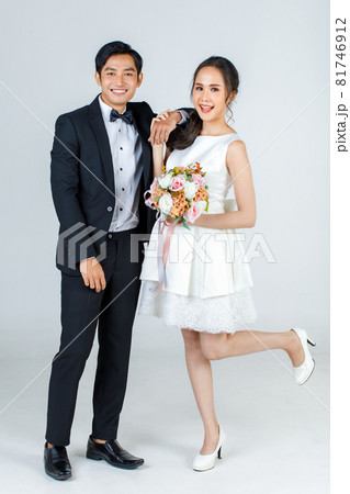 Young attractive Asian couple, bride and groom, woman wearing white wedding dress holding bouquet of flower. Man wearing black tuxedo, standing together. Concept for pre wedding photography 81746912