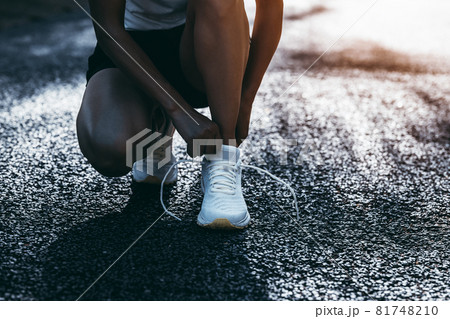 Woman runner tying shoelace on sunny tropical park trail Woman runner tying shoelace on sunny tropical park trail 81748210