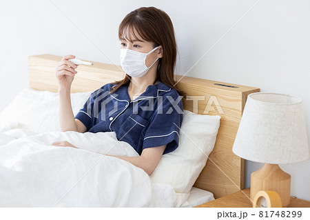 体調不良　ベッドで体温を測る若い女性 81748299