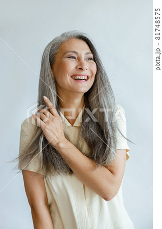 Middle aged Asian woman touches natural hoary hair on light grey background Middle aged Asian woman touches natural hoary hair on light grey background 81748575