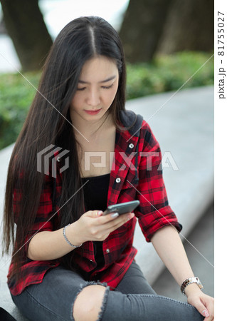 Female teenager sitting in city street, messaging to her friends, using smartphone 81755027