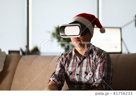 Man in virtual glasses sits on sofa wearing santa claus hat Man in virtual glasses sits on sofa wearing santa claus hat 81756233