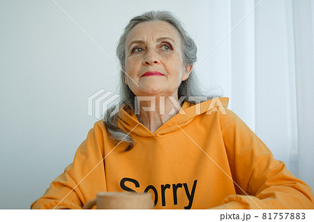 Close-up portrait of pensive and calm mature woman with gray hair and holding a coffee mug 81757883