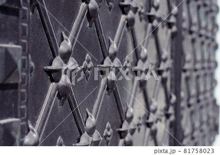 Massive antique black metal door. Surface with repeating ornamentation. Wrought rhombus and geometric pattern. Selective focus. Side view. Outside. 81758023