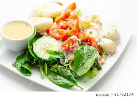 Healthy salad, potato salad with hard boiled egg, shredded ham, cucumber, tomatoes, lettuce and spinach with a honey and mustard dressing pot 81762174