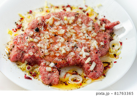 Minced meat with fresh spring onions and spices in the shape of a pig on the white plate, a creatively prepared burger in an interesting shape Minced meat with fresh spring onions and spices in the shape of a pig on the white plate, a creatively prepared burger in an interesting shape 81763365