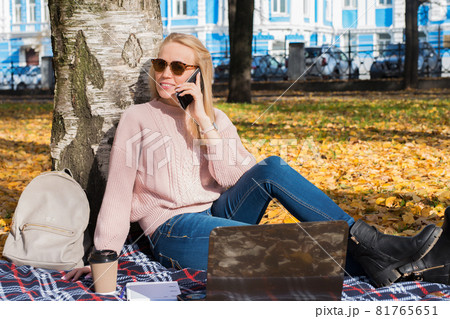 Young woman working with laptop outdoors and holding phone 81765651