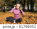 A young woman plays sports outside in an autumn park and listens to music with headphones 81766052