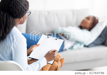 Black female patient lying on sofa at psychologist's office, having session with counselor, getting depression treatment Black female patient lying on sofa at psychologist's office, having session with counselor, getting depression treatment 81769796