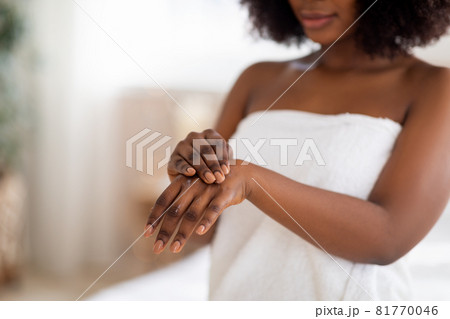 Unrecognizable young Afro lady applying hand cream after shower, wearing white towel indoors, copy space 81770046