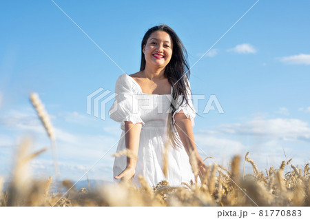 Young Woman in white dress standing on golden wheat field at sunny day, touching gently the wheat. Young Woman in white dress standing on golden wheat field at sunny day, touching gently the wheat. 81770883