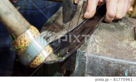 blacksmith hits the blade of scythe by hammer in rural workshop 81770961