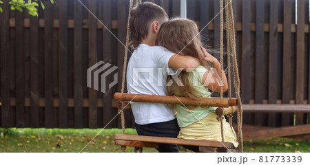 children sitting on a swing in the garden. older brother hugging little sister 81773339