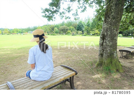 広い公園のベンチに座った女の子の後ろ姿の写真素材