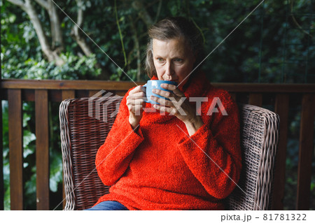 Thoughtful senior caucasian woman sitting on chair, drinking coffee in garden 81781322