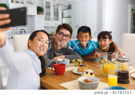 Smiling asian parents with son and daughter sitting at breakfast table taking selfie Smiling asian parents with son and daughter sitting at breakfast table taking selfie 81781551