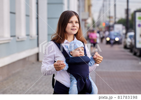 Young woman uses baby carrier or sling while walking outside with her four month old son. Young woman uses baby carrier or sling while walking outside with her four month old son. 81783198