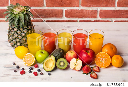 Different fruits juice in glass, apple, orange and strawberry juice with straw, looking refreshing on colourful wood board in front of brick wall background. Picture decorating with fresh fruits Different fruits juice in glass, apple, orange and strawberry juice with straw, looking refreshing on colourful wood board in front of brick wall background. Picture decorating with fresh fruits 81783901