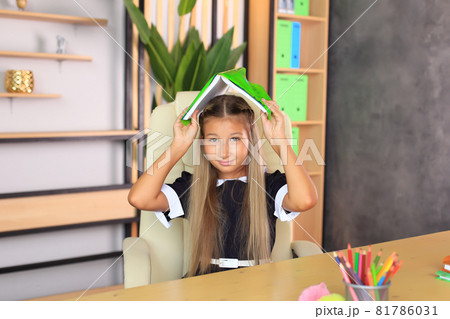 Portrait of a girl in a school uniform with a book in her hands. The child reads a textbook. Preparing a schoolgirl for a school lesson or exam Portrait of a girl in a school uniform with a book in her hands. The child reads a textbook. Preparing a schoolgirl for a school lesson or exam 81786031