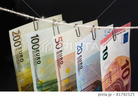 Parts of different euro bills are hanging on clerical clips on a rope on the dark background. Closeup, selective focus Parts of different euro bills are hanging on clerical clips on a rope on the dark background. Closeup, selective focus 81792525