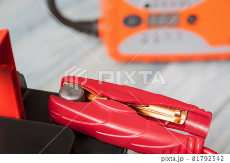 A car battery with red and black battery jumper clamps and car battery charger on the background. Closeup, selective focus 81792542