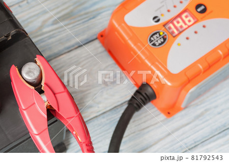A car battery with red and black battery jumper clamps and a car battery charger. Closeup, selective focus 81792543