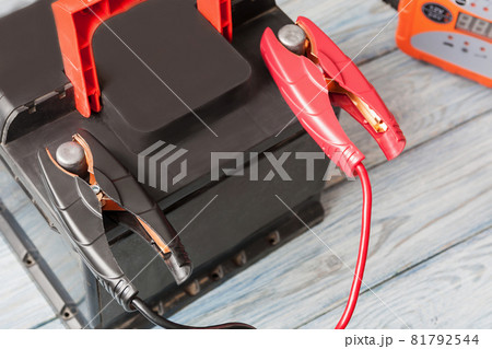 A car battery with red and black battery jumper clamps and car battery charger on the background. Closeup, selective focus 81792544