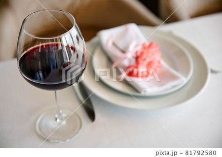 Glass of red wine on background of served table in a restaurant. Close-up, selective focus Glass of red wine on background of served table in a restaurant. Close-up, selective focus 81792580