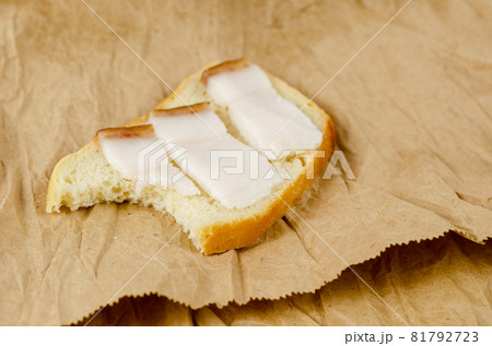 Sandwich bite on a brown background. Sandwich with salted lard. Three slices of pork fat with burnt skin and a slice of wheat bread. Brown paper bag. Sandwich bite on a brown background. Sandwich with salted lard. Three slices of pork fat with burnt skin and a slice of wheat bread. Brown paper bag. 81792723