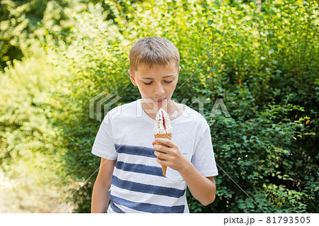 Teenager boy eating ice-cream cone on green nature background. Summer, junk food and people concept 81793505