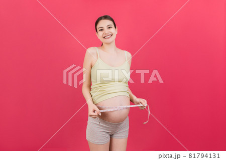 pregnant woman measuring her growing abdomen at colored background. Inch tape measure. Copy space pregnant woman measuring her growing abdomen at colored background. Inch tape measure. Copy space 81794131