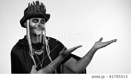Sinister man with horrible Halloween skeleton makeup ooking at camera, pointing to the left 81795013