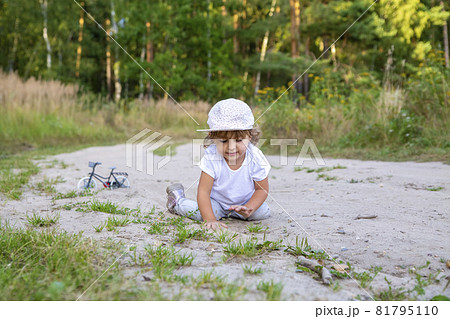 cute happy toddler in a cap crawls on all fours along a country road in the sand on a sunny summer day 81795110