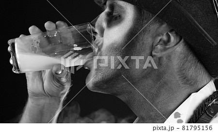 Creepy man with skeleton makeup in white shirt. Guy looking at camera, drinks milk from a glass Creepy man with skeleton makeup in white shirt. Guy looking at camera, drinks milk from a glass 81795156