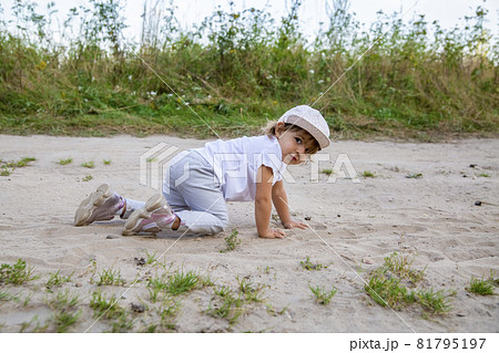 cute happy toddler in a cap crawls on all fours along a country road in the sand on a sunny summer day 81795197