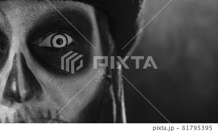 Close-up shot of face in skeleton Halloween makeup opening eyes with white pupil, trying to scare 81795395