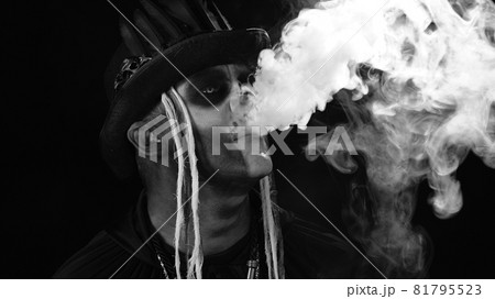Sinister man with professional skull makeup exhaling cigarette smoke from his mouth and nose Sinister man with professional skull makeup exhaling cigarette smoke from his mouth and nose 81795523