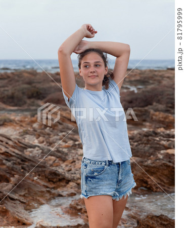 Teenage girl standing on cliff by the sea Teenage girl standing on cliff by the sea 81795999
