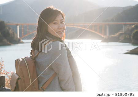 夕日の反射する宮ヶ瀬湖をバックに立つ女性 81800795