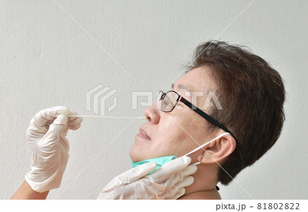 elder woman wearing eye glasses testing by hand in glove holding cotton bud and antigen test kit for checking COVID-19 or coronavirus on white background 81802822