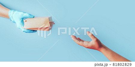 Hand in blue glove passes paper food container to the other hand against blue background 81802829
