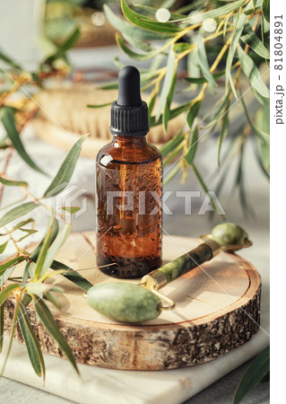 Amber glass transparent bottle with Jade face roller and eucalyptus leaves. Skin Care Anti-Aging concept, face massage Amber glass transparent bottle with Jade face roller and eucalyptus leaves. Skin Care Anti-Aging concept, face massage 81804891