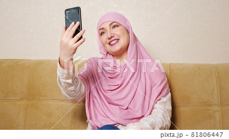 Beautiful muslim woman in hijab talking by video call while sitting on the couch 81806447