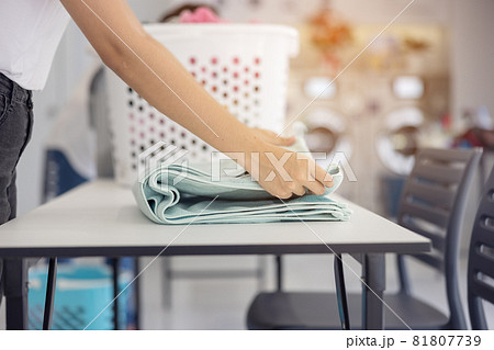In the self-service laundry with dryer machines in the backdrop, a young woman enjoys clean ironed garments. In the self-service laundry with dryer machines in the backdrop, a young woman enjoys clean ironed garments. 81807739