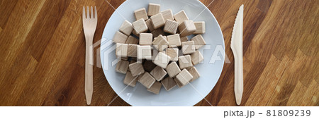 Wooden cubes lying on plate near knife and fork closeup Wooden cubes lying on plate near knife and fork closeup 81809239