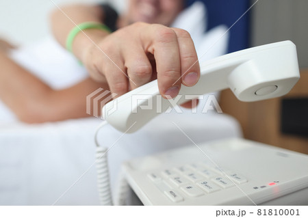 Man hand picking up receiver of phone in bedroom closeup Man hand picking up receiver of phone in bedroom closeup 81810001