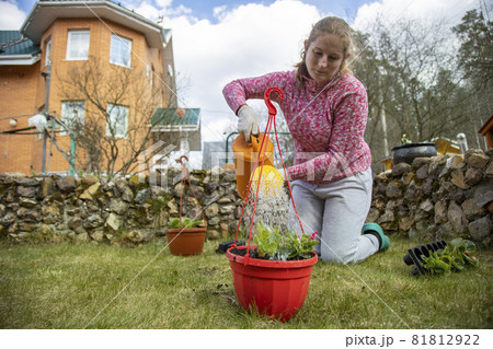woman watering potted flowers from a garden watering can in the backyard of a house in spring 81812922
