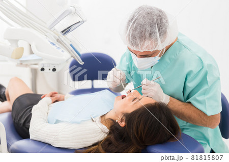 Dentist man examining a latin female patient teeth 81815807
