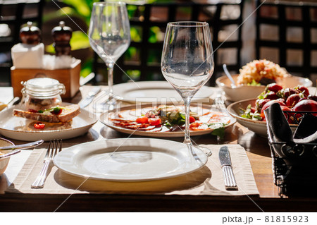 wooden table served with plates with salad and snacks on the open terrace wooden table served with plates with salad and snacks on the open terrace 81815923